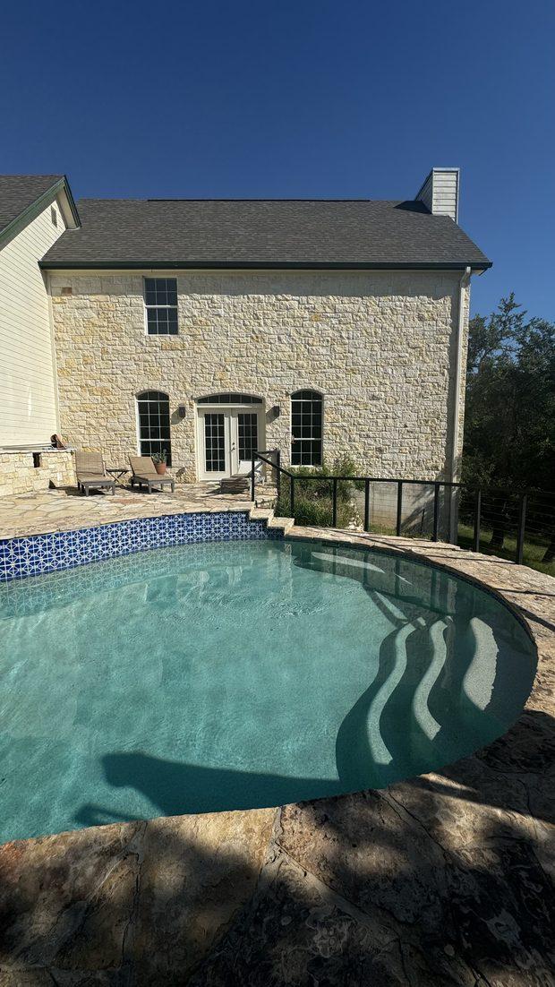 A curved swimming pool beside a limestone house